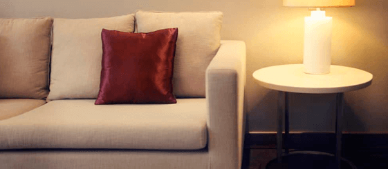 beige sofa with pillows and a tablet with a candle next to it