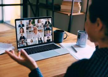 open laptop on a wooden table showing people on a conference call