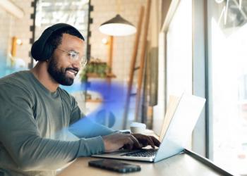 black men working on his laptop sitting on a chair at a table