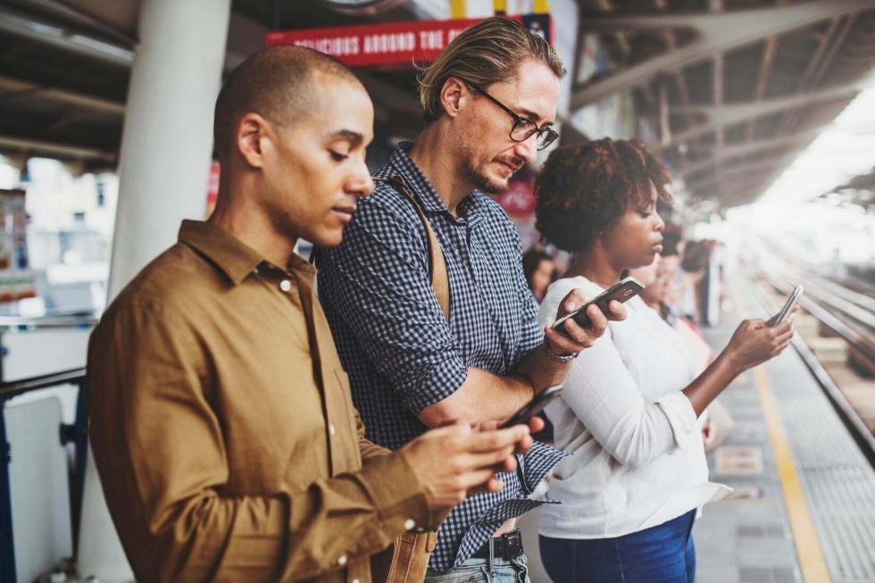 3 people looking at their phone at a train station